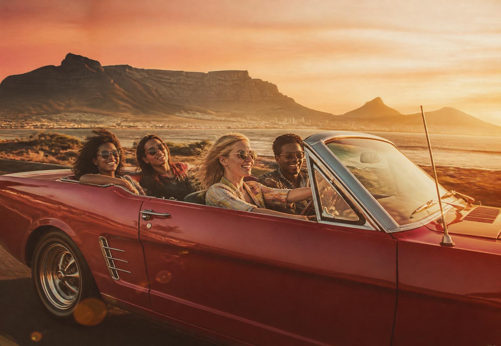 Friends on a Cape Town road trip in a red convertible at sunset